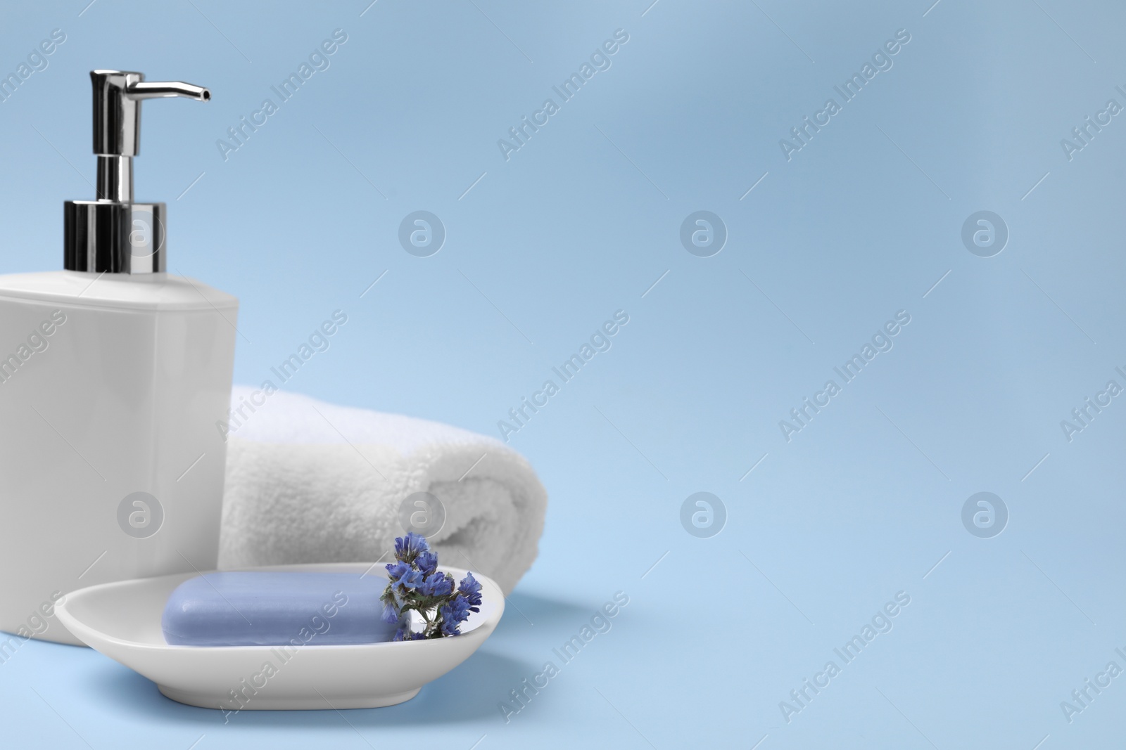 Photo of Soap bar, bottle dispenser and towel on light blue background, space for text