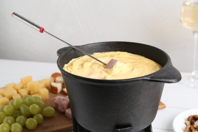 Dipping ham into fondue pot with tasty melted cheese at table, closeup