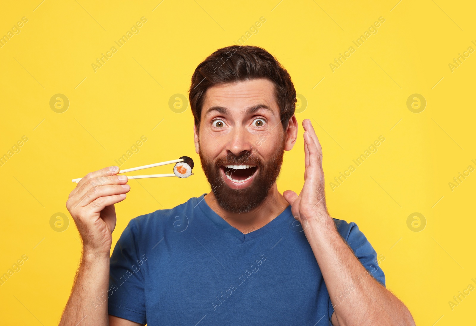 Photo of Emotional man holding sushi roll with chopsticks on orange background