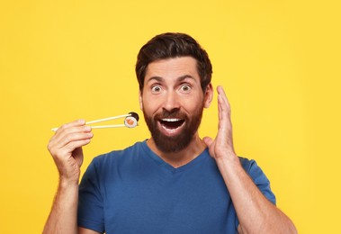 Photo of Emotional man holding sushi roll with chopsticks on orange background