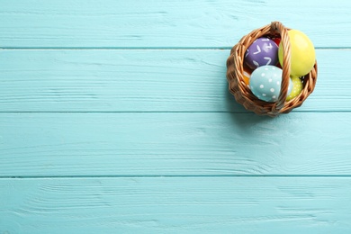 Wicker basket with painted Easter eggs on wooden table, top view. Space for text