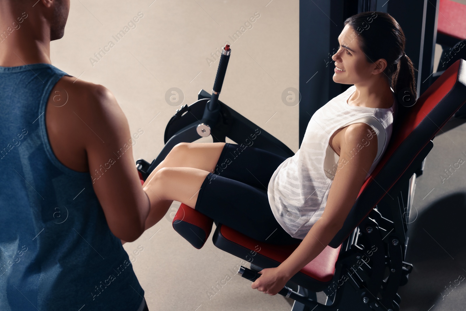 Photo of Young woman working out with professional trainer in modern gym