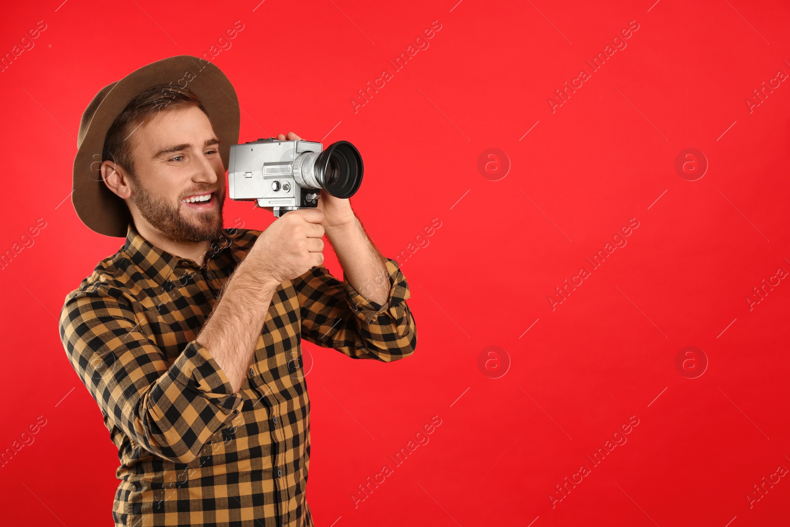 Photo of Young man with vintage video camera on red background. Space for text