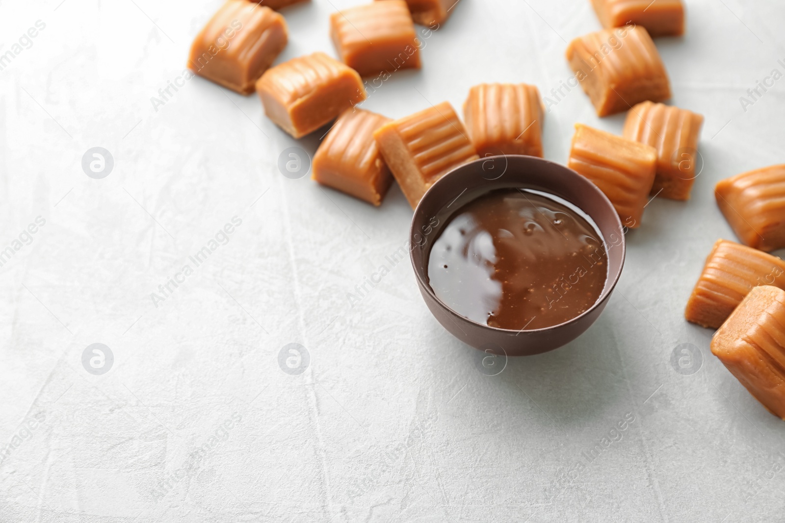 Photo of Delicious caramel candies and sauce on light background