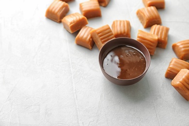 Delicious caramel candies and sauce on light background