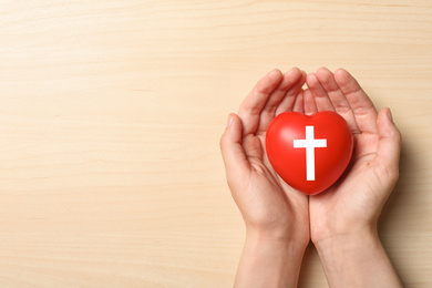 Woman holding heart with cross symbol on beige background, top view with space for text. Christian religion