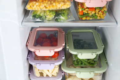 Plastic bags and containers with different frozen vegetables in refrigerator