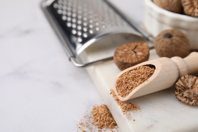 Photo of Scoop with grated nutmeg, seeds and grater on white table, closeup. Space for text