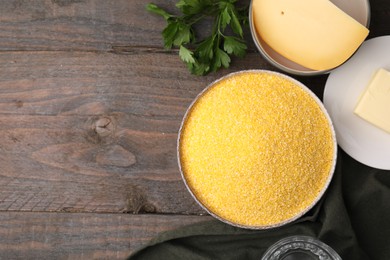 Raw cornmeal in bowl, parsley, cheese and butter on wooden table, flat lay. Space for text