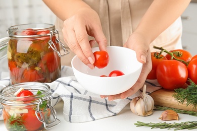 Photo of Woman putting pickled tomato into bowl in kitchen, closeup view