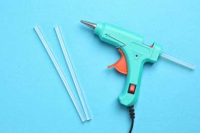 Photo of Turquoise glue gun and sticks on light blue background, flat lay