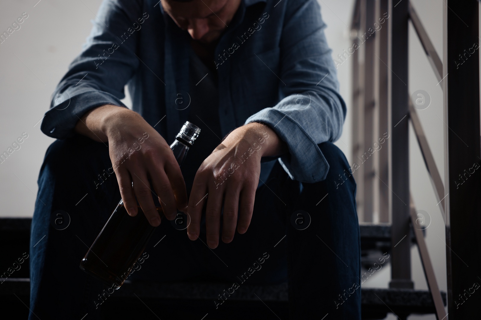 Photo of Addicted man with alcoholic drink on stairs indoors, closeup