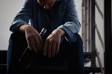 Addicted man with alcoholic drink on stairs indoors, closeup