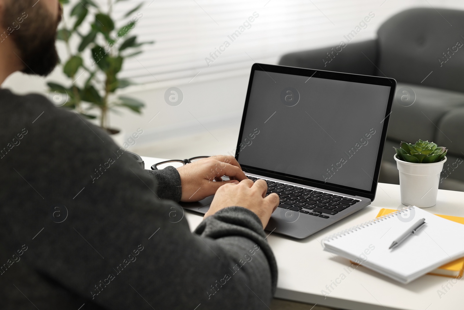 Photo of E-learning. Young man using laptop at white table indoors, closeup