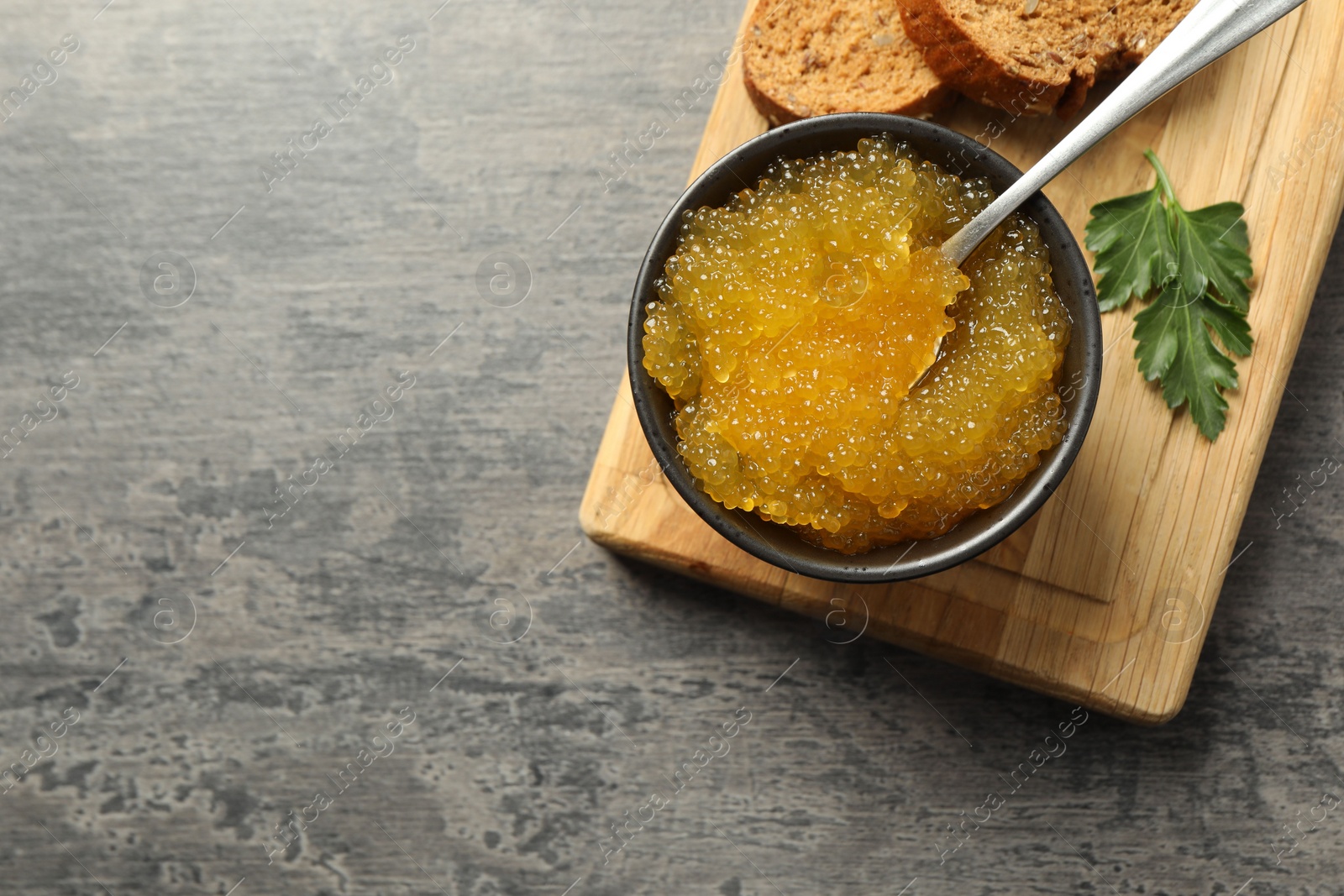 Photo of Fresh pike caviar in bowl, parsley and bread on grey table, top view. Space for text