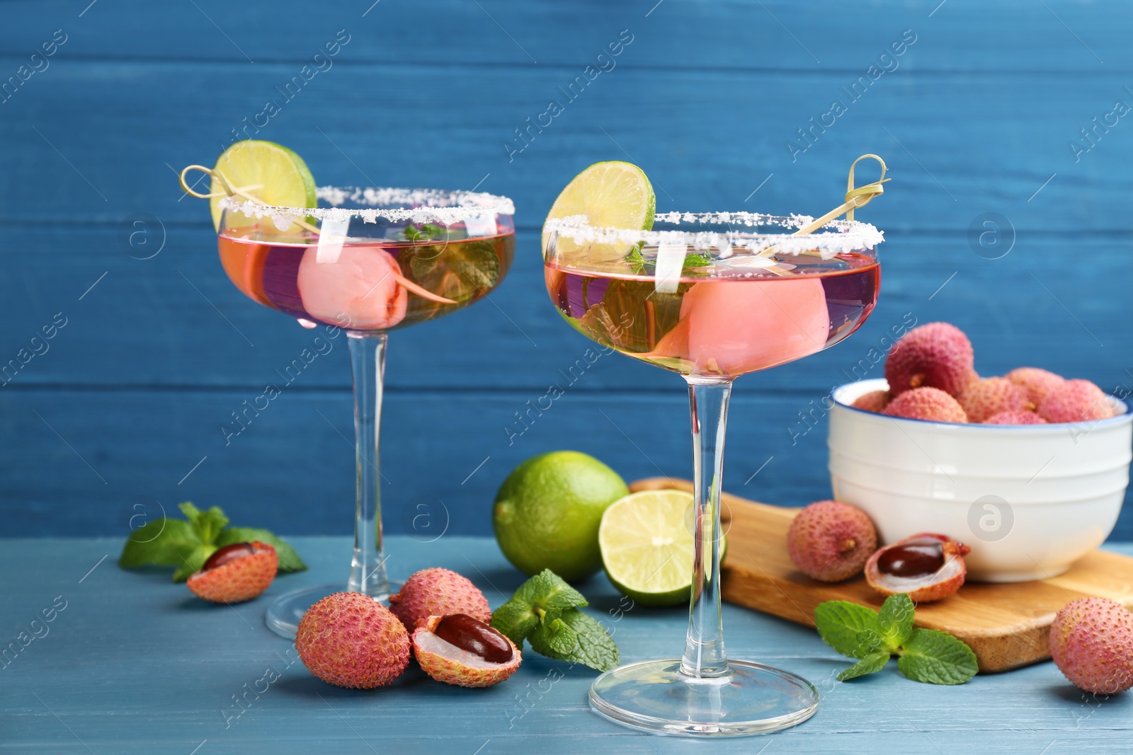 Photo of Lychee cocktail with lime and fresh fruits on light blue table
