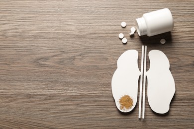 Paper cutout, sand and pills on wooden table, flat lay with space for text. Kidney stone disease