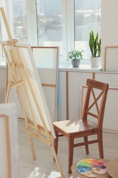 Photo of Easel with canvas and chair near window in artist's studio. Creative hobby
