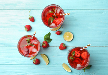 Photo of Refreshing drink with strawberry and lime on light blue wooden table, flat lay
