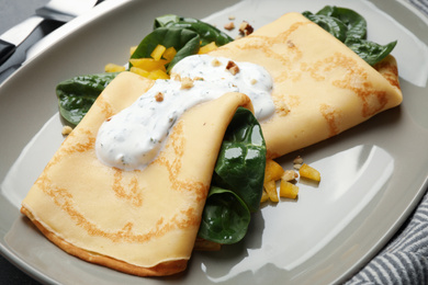 Photo of Delicious thin pancakes with spinach and sour cream on plate, closeup