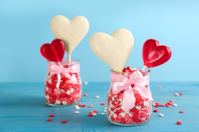 Heart shaped lollipops made of chocolate and sugar syrup with sprinkles on light blue background