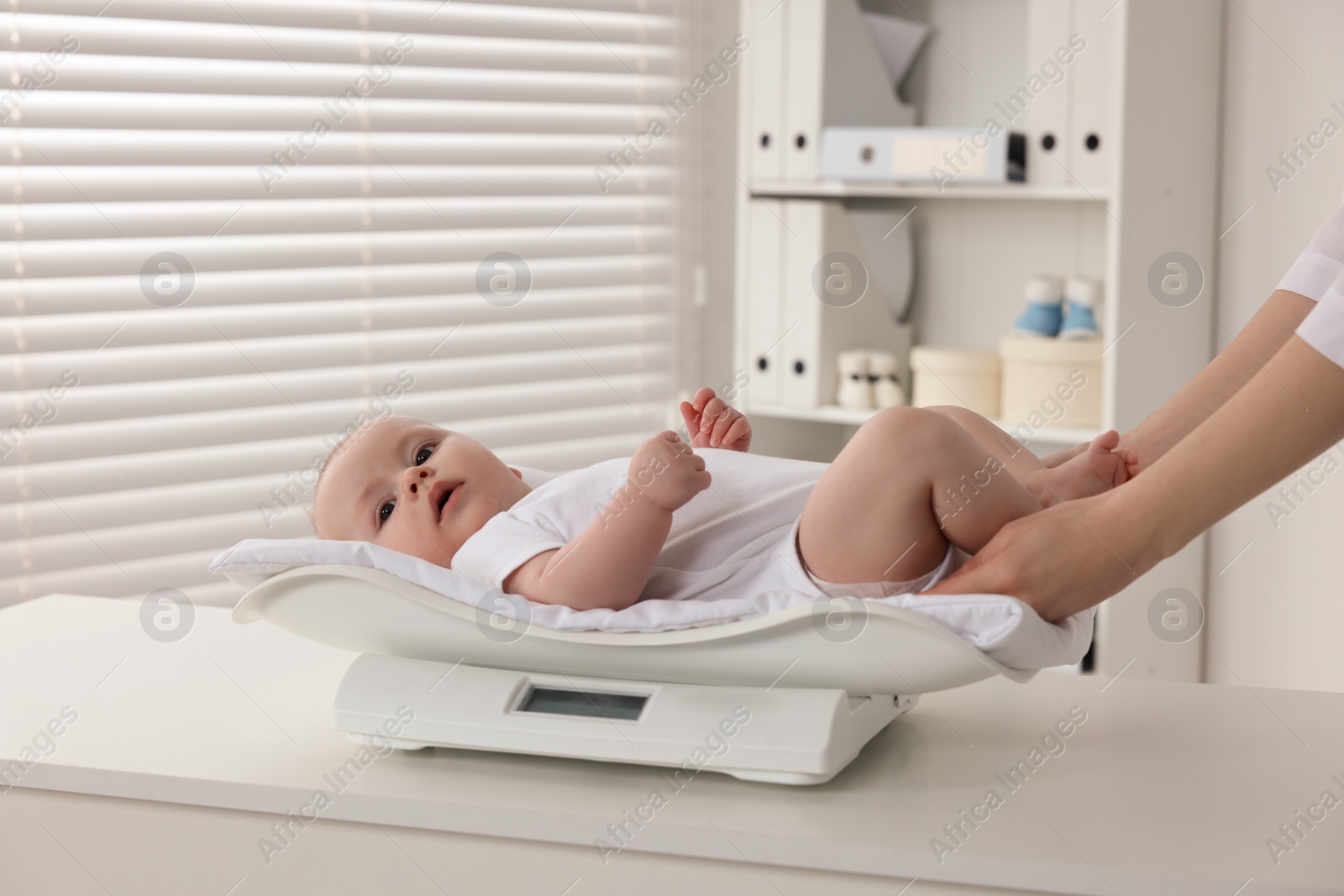 Photo of Pediatrician weighting cute little baby in clinic, closeup