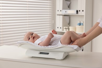 Photo of Pediatrician weighting cute little baby in clinic, closeup