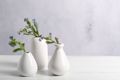 Photo of Beautiful forget-me-not flowers in vases on white marble table, closeup. Space for text
