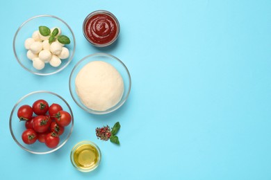 Photo of Raw dough and other pizza ingredients on light blue background, flat lay. Space for text