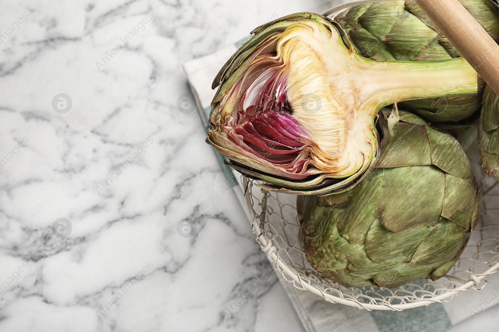 Photo of Cut and whole fresh raw artichokes on white marble table, top view. Space for text