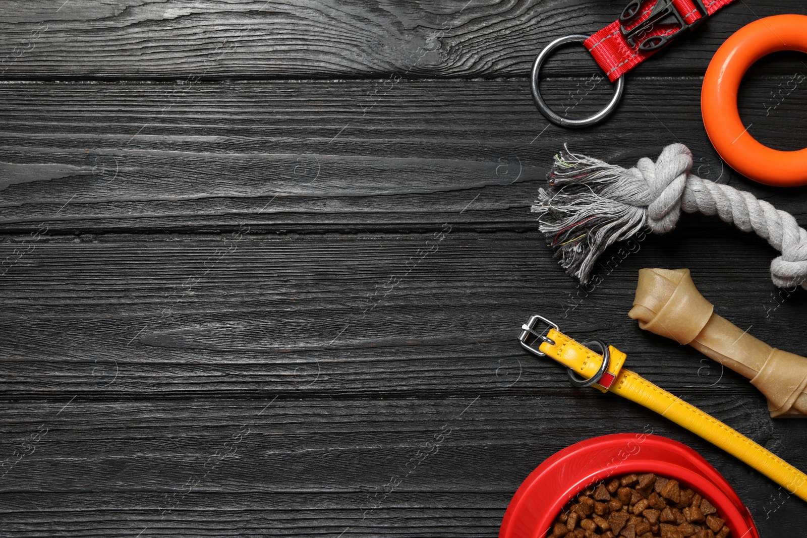 Photo of Flat lay composition with dog collar, toys and food on black wooden table. Space for text