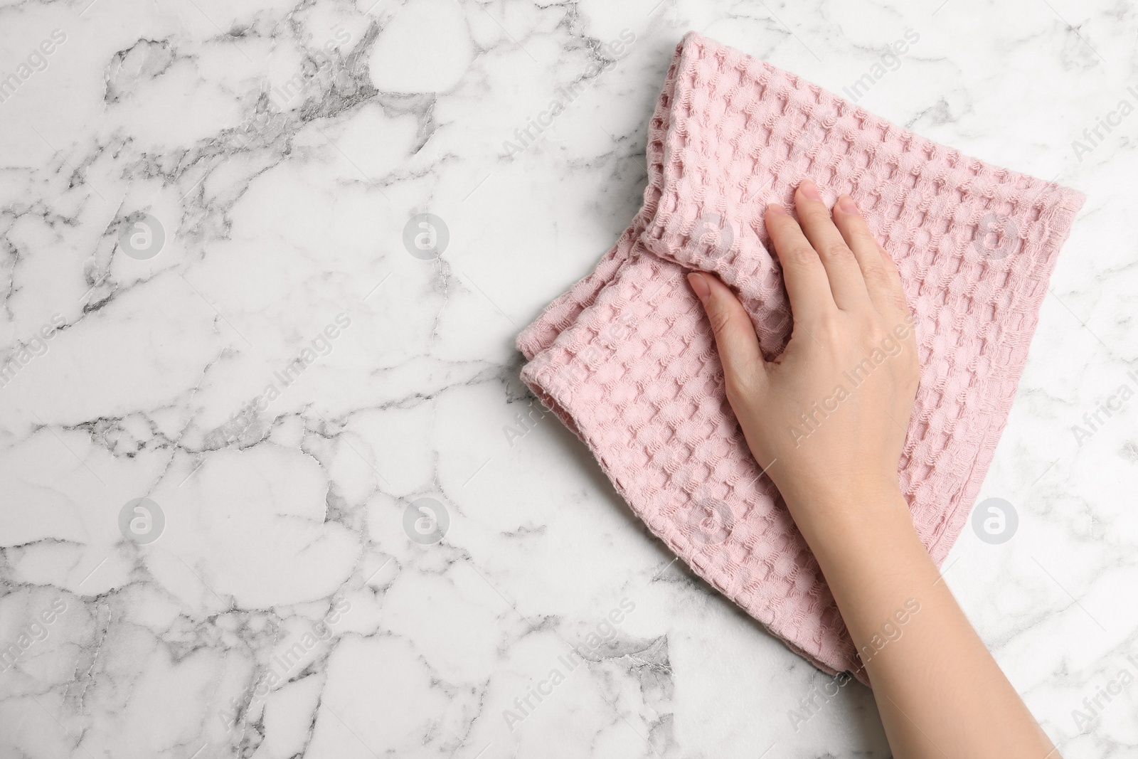 Photo of Woman wiping white marble table with kitchen towel, top view. Space for text