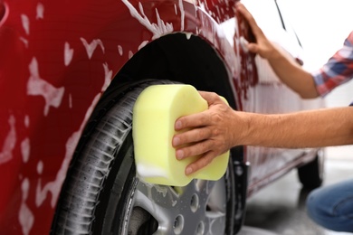 Photo of Man washing red auto with sponge at car wash, closeup