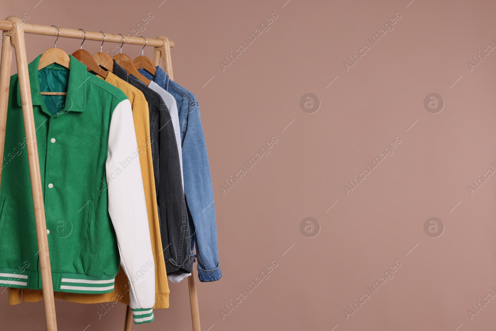 Photo of Rack with stylish clothes on wooden hangers against beige background, space for text