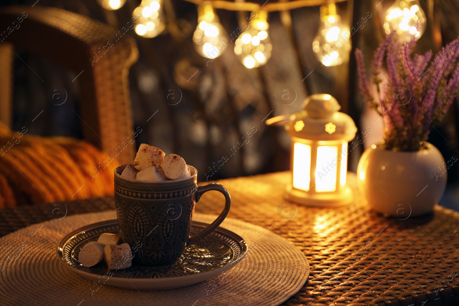 Photo of Cup with tasty cocoa and marshmallows on rattan table at balcony in evening. Space for text