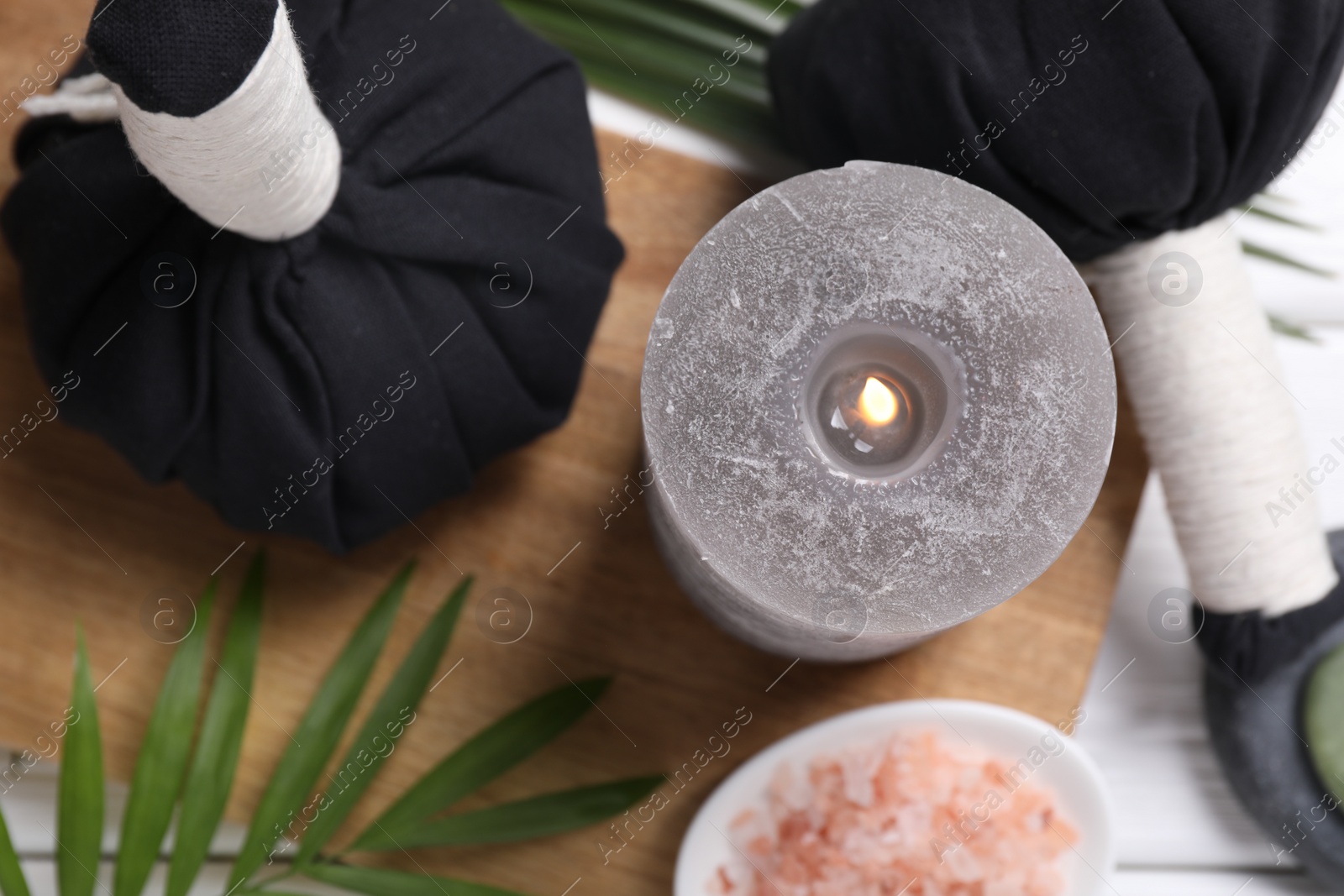 Photo of Beautiful spa composition with herbal massage bags, burning candle and leaves on white wooden table, flat lay