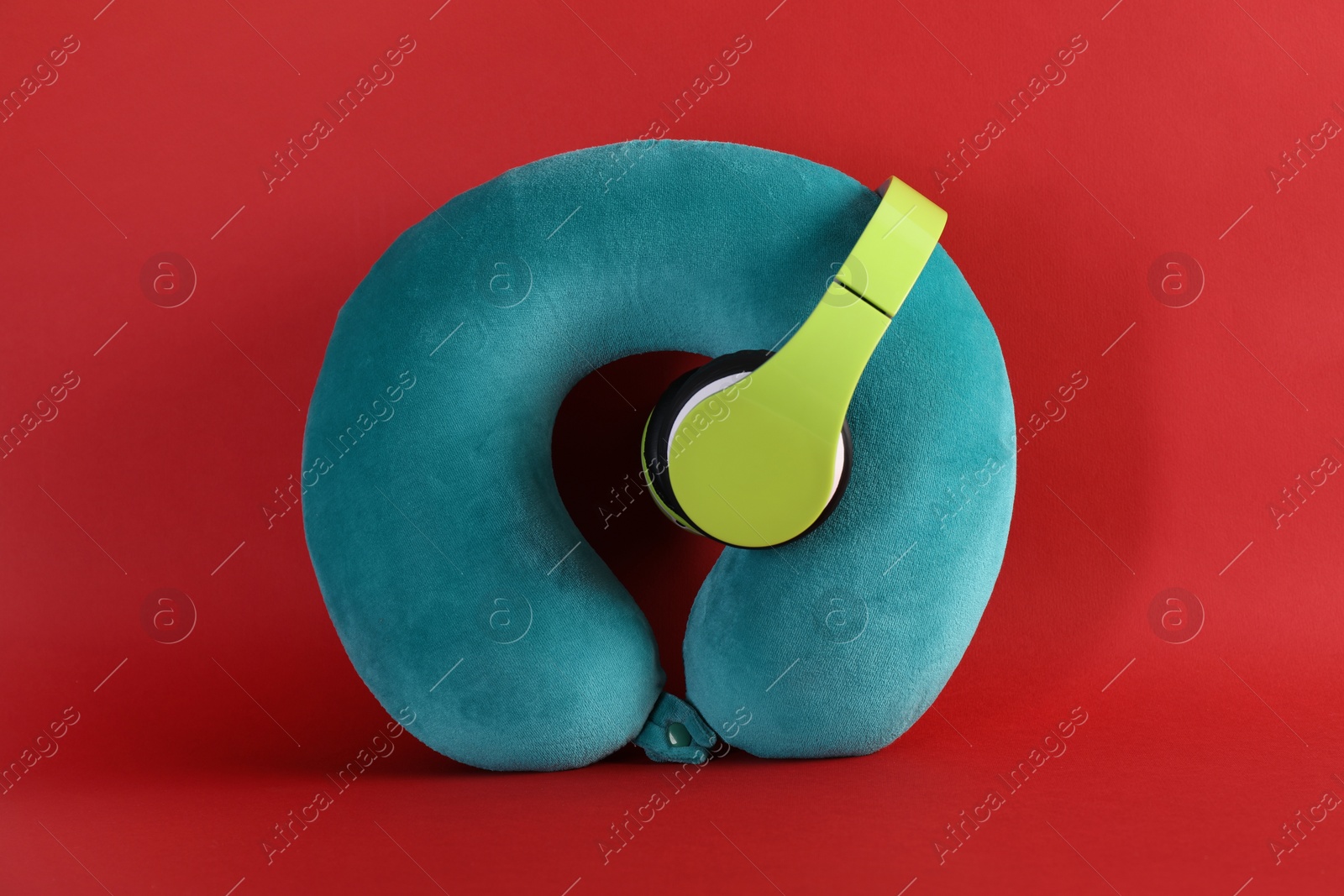 Photo of Turquoise travel pillow and headphones on red background