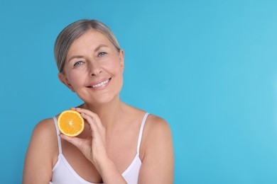 Beautiful woman with half of orange rich in vitamin C on light blue background, space for text
