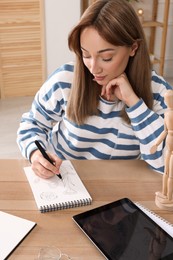 Photo of Woman drawing in sketchbook with pen at wooden table indoors