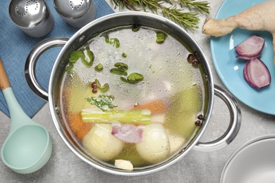 Pot with tasty bouillon and different ingredients on light grey table, flat lay