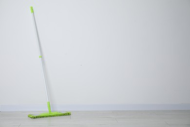 Mop with plastic handle near wall indoors. Space for text