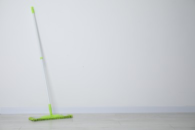 Photo of Mop with plastic handle near wall indoors. Space for text