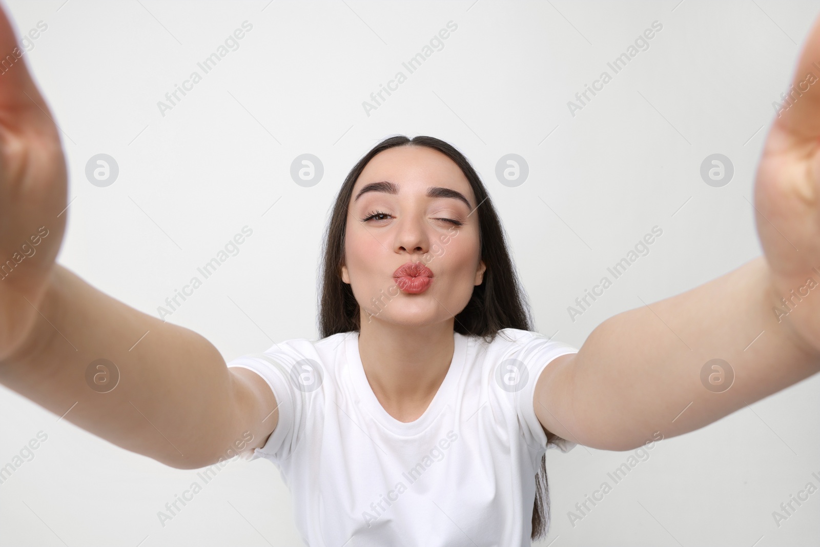 Photo of Young woman taking selfie and blowing kiss on white background