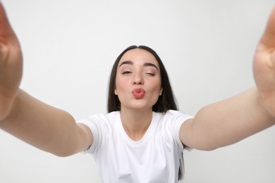 Young woman taking selfie and blowing kiss on white background