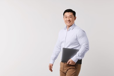 Portrait of happy man with laptop on light background. Space for text