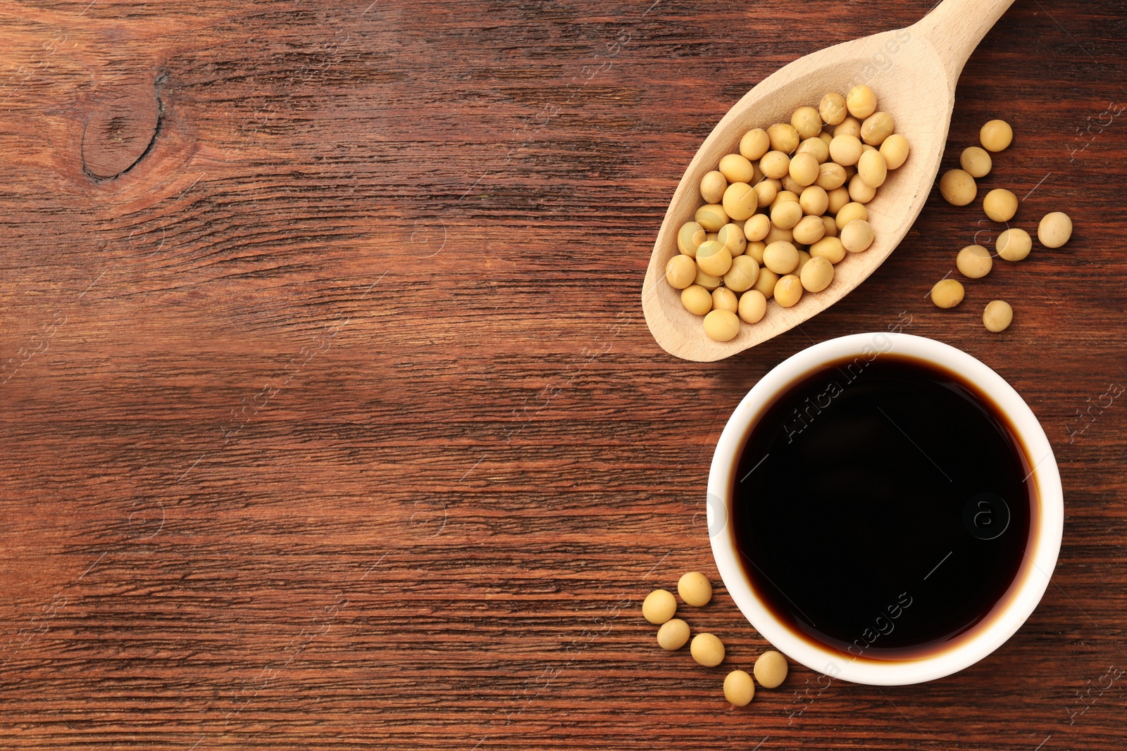 Photo of Soy sauce in bowl and soybeans on wooden table, flat lay. Space for text