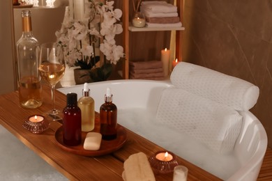 Photo of Tub with soft bath pillow, toiletries and wine indoors