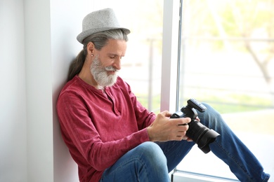 Male photographer with professional camera on window sill indoors
