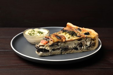 Piece of delicious quiche with mushrooms and sauce on wooden table