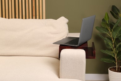 Photo of Laptop on sofa armrest wooden table in room. Interior element